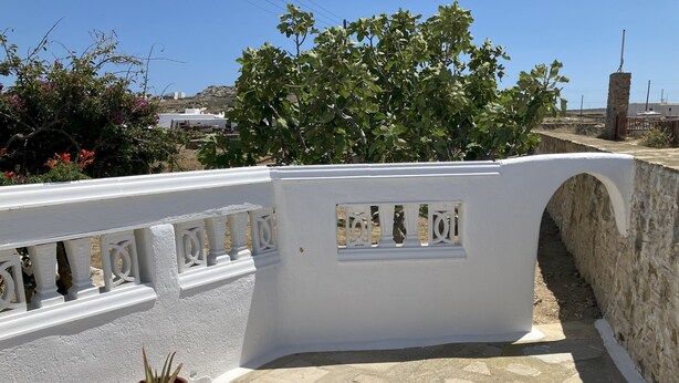 A white balcony with a stone floor, potted plants, and a view of a hillside with buildings. - LINA'S HOUSE (Mykonos)
