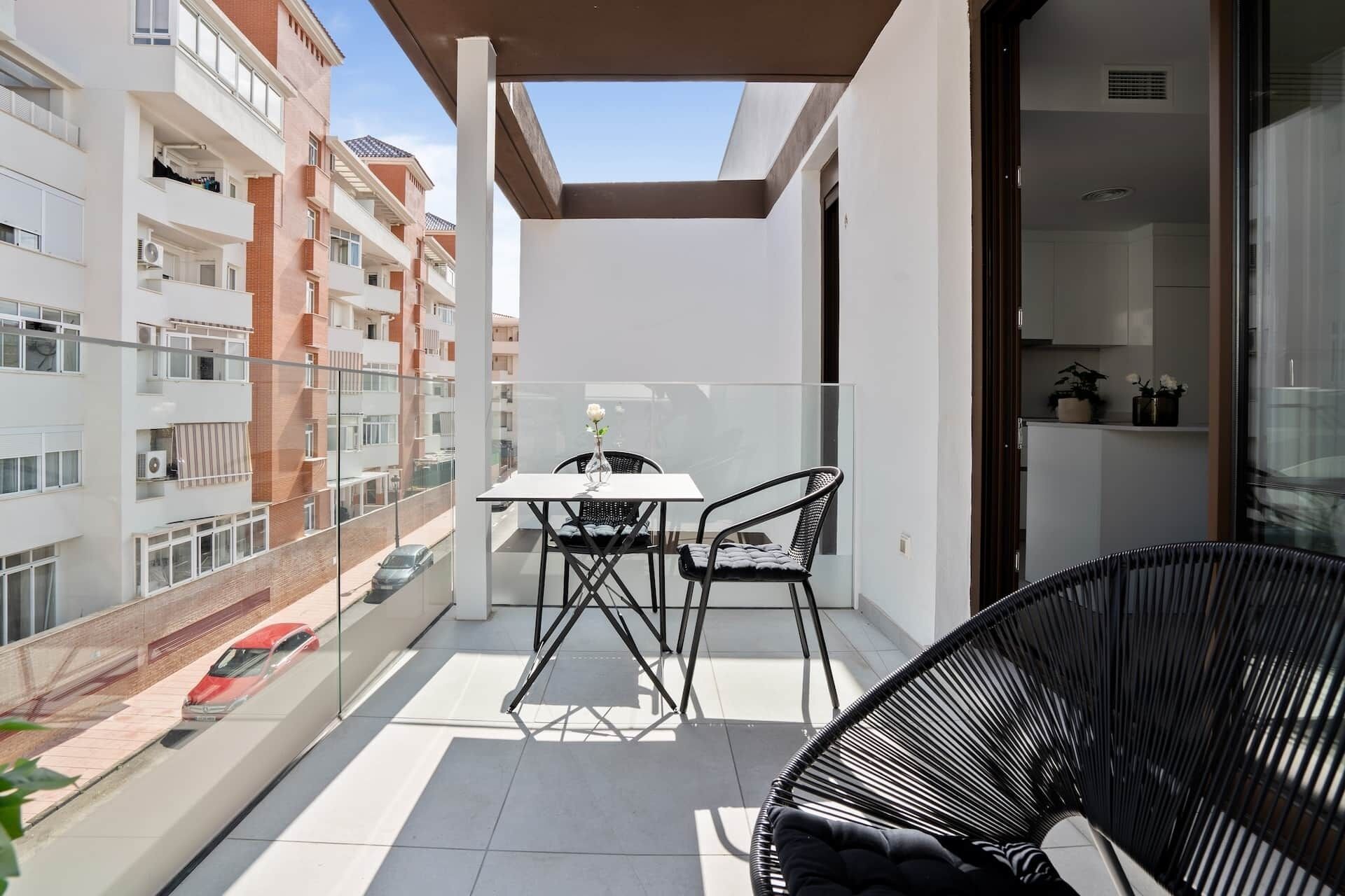Un balcone con tavolo e sedie, una porta vetrata e vista sugli edifici vicini.