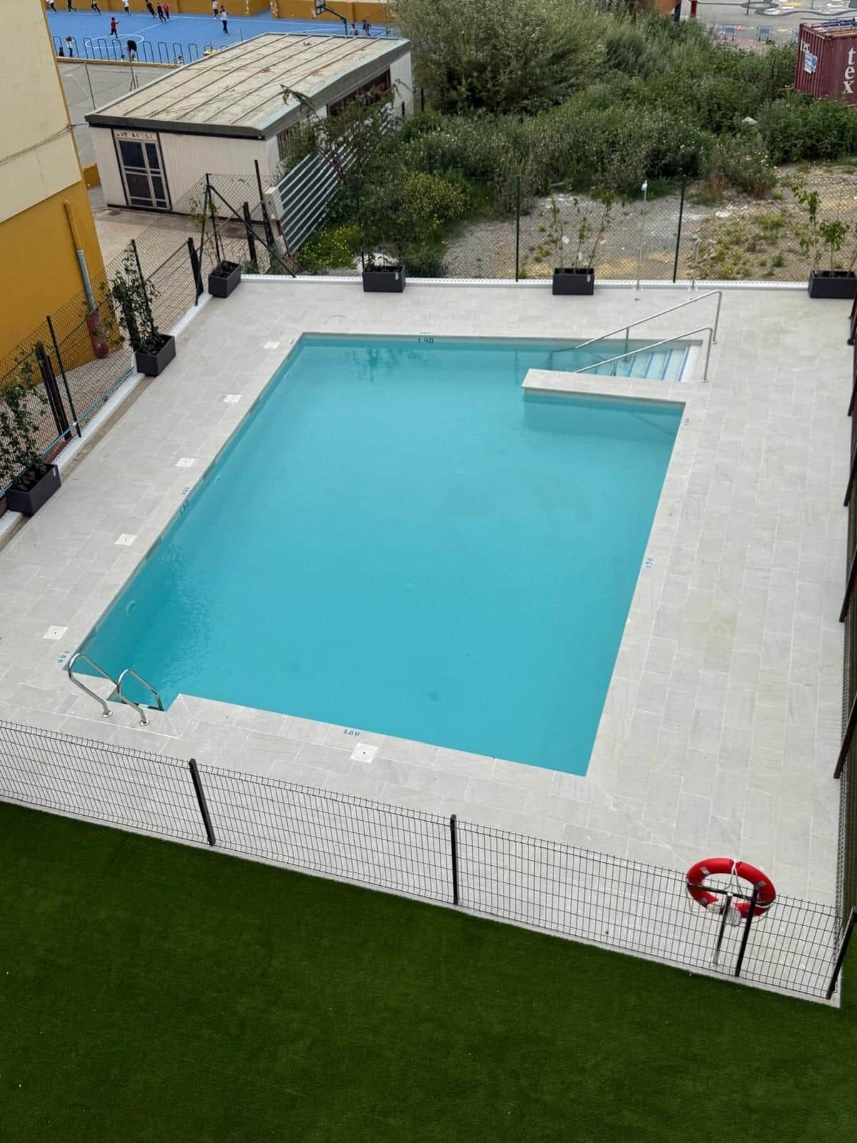 Una piscina rectangular con solárium empedrado, rodeada por una valla y un flotador salvavidas.