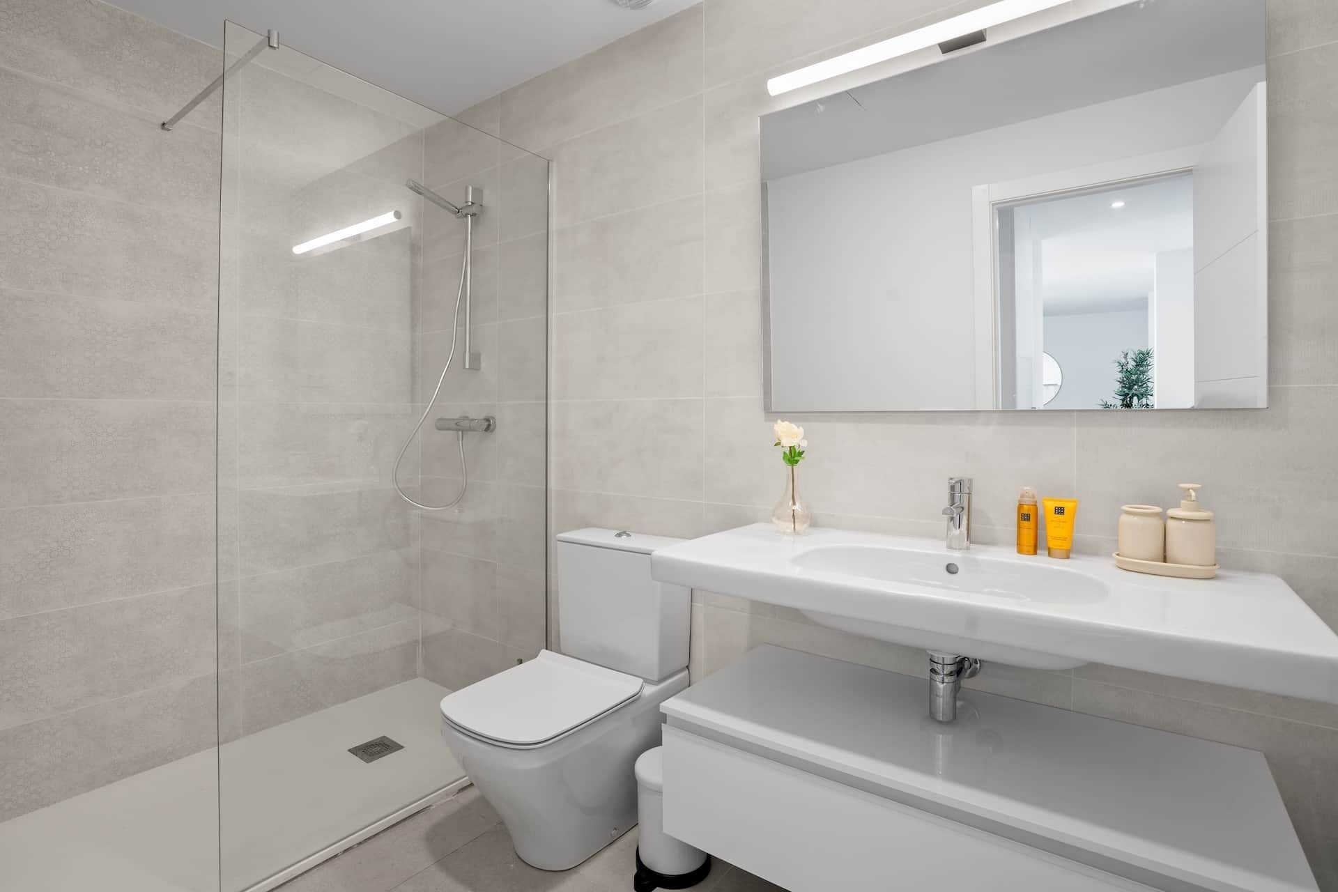 Un baño moderno con ducha envuelta en vidrio, inodoro blanco y tocador con espejo.