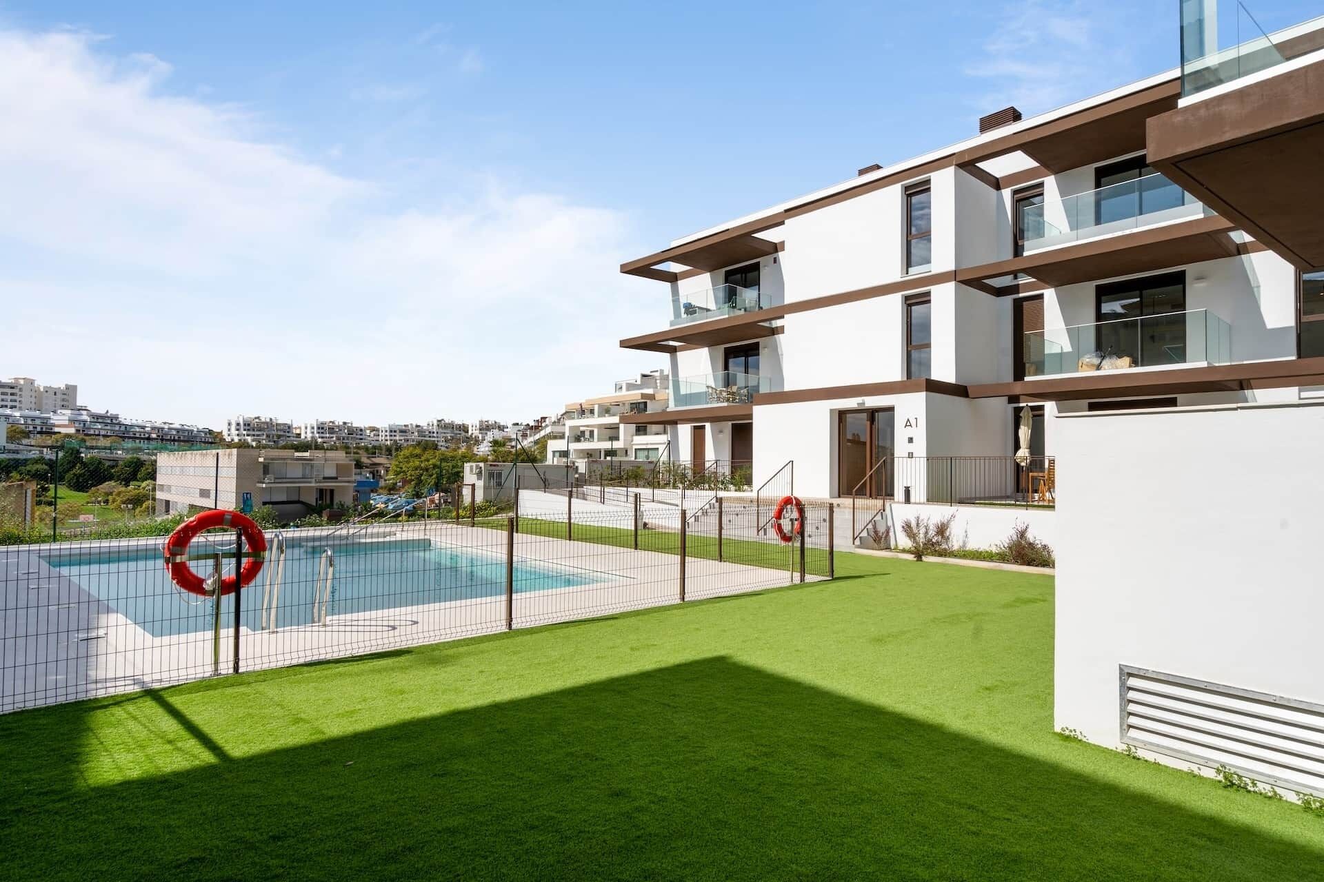 A modern apartment with a swimming pool, a grassy lawn, and a view of the cityscape.