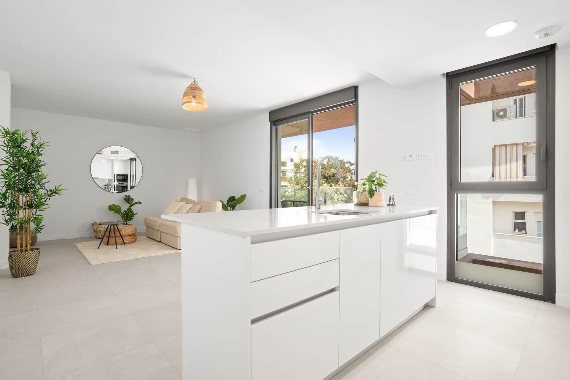 A modern kitchen with a central island, a dining area with a sofa and chairs, and a large window providing a view of the outside.
