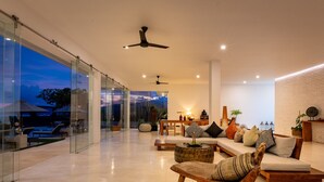 Ein geräumiges Wohnzimmer mit einer großen Glasschrankwand, einem Deckenventilator und einer gemütlichen Sitzecke mit Sofa und Sesseln.