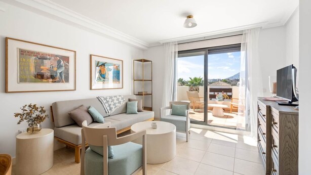 A modern living room with a sofa, chairs, a coffee table, and a TV on a wooden cabinet. There are two framed pictures on the wall and a balcony with outdoor furniture. - RDR487 - Modern Duplex Penthouse in gated complex (Estepona)