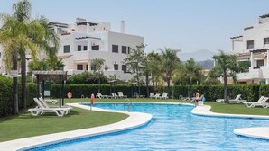 A swimming pool with lounge chairs and a lifebuoy, surrounded by greenery and buildings. - RDR487 - Modern Duplex Penthouse in gated complex (Estepona)