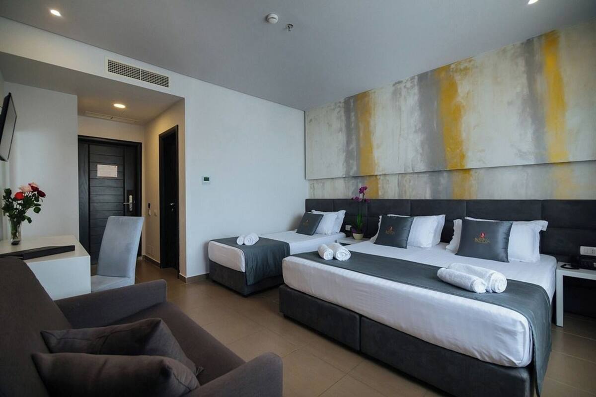 Ein Hotelzimmer mit zwei Betten, einem Sofa, einem Schreibtisch und einem großen, abstrakten Gemälde an der Wand.