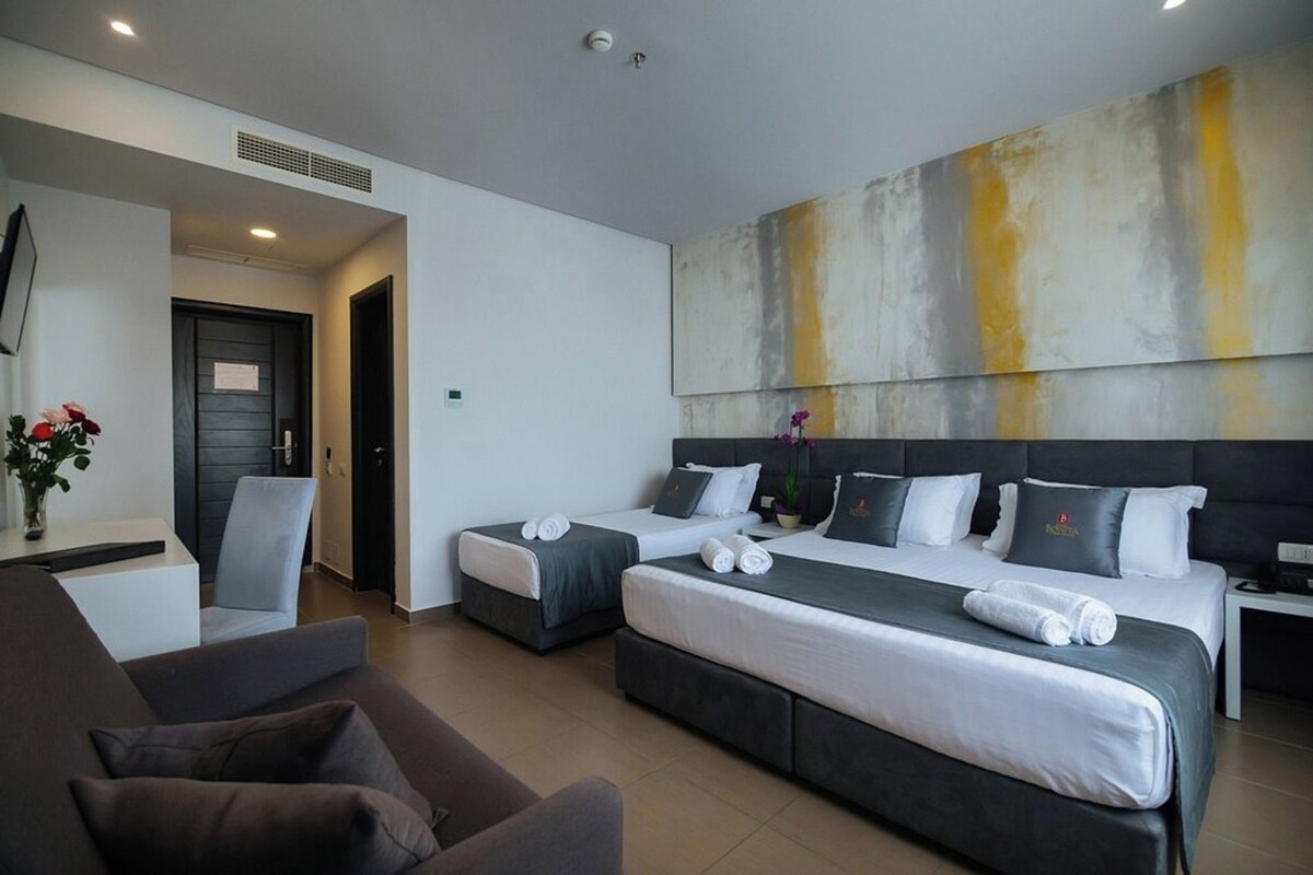 Une chambre d’hôtel avec deux lits, un canapé, un bureau et un grand tableau abstrait accroché au mur.