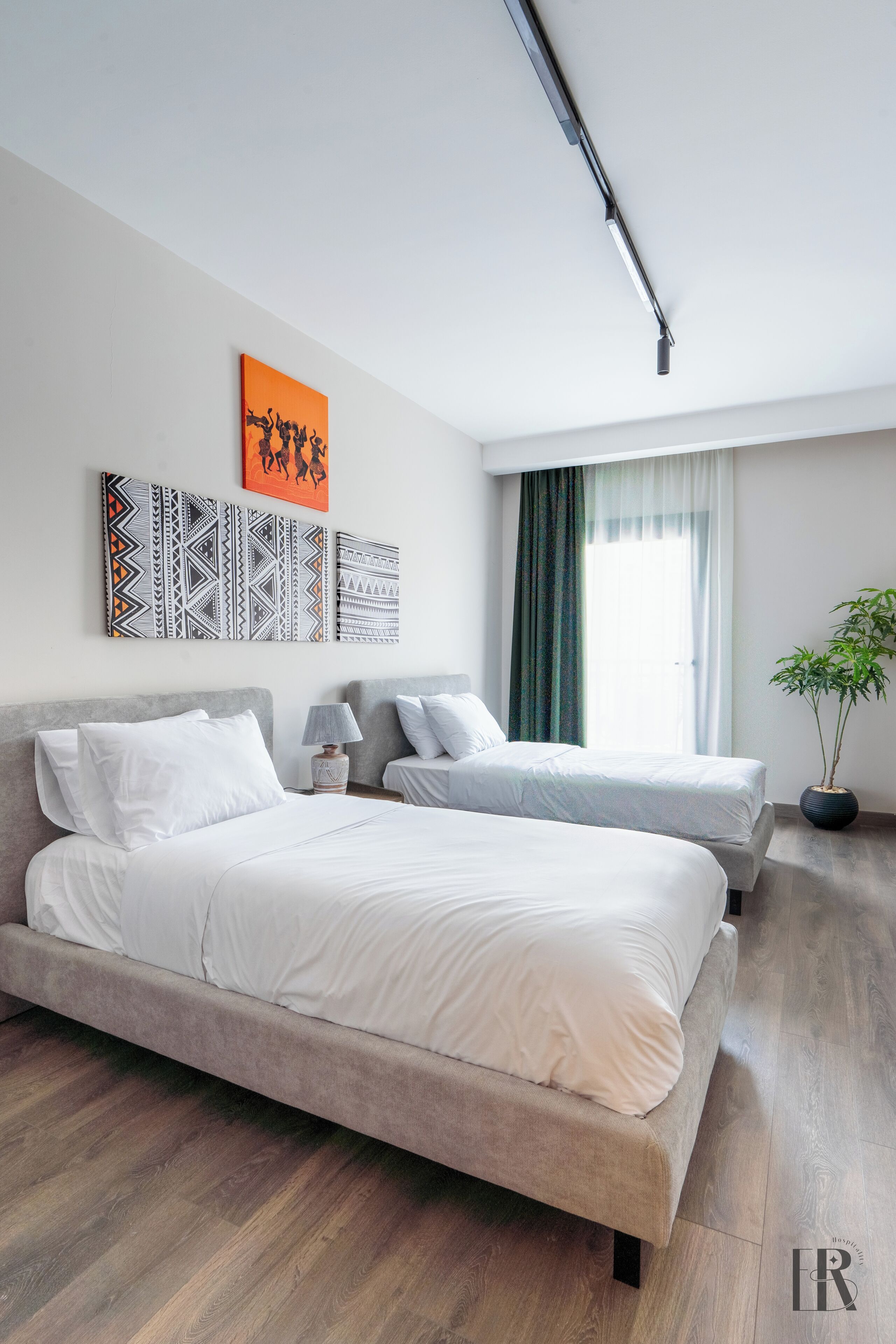A modern hotel room with two beds, a large window with curtains, and a wall with patterned artwork.