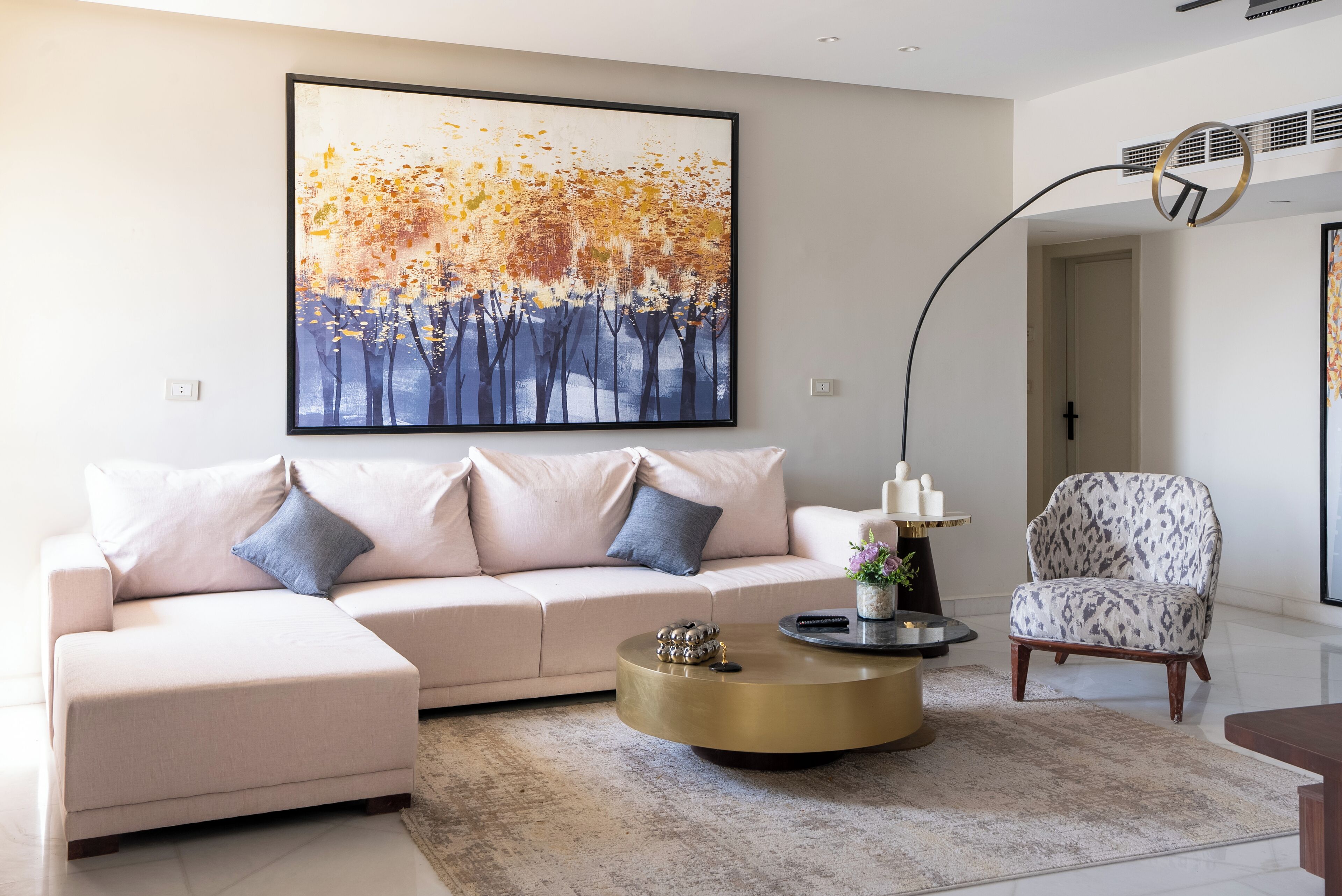 A modern living room with a beige sofa, a round coffee table, and a patterned armchair.