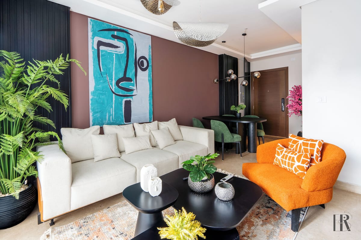 A modern living room with a sofa, coffee table, and orange armchair. There is a large abstract painting on the wall and a potted plant.