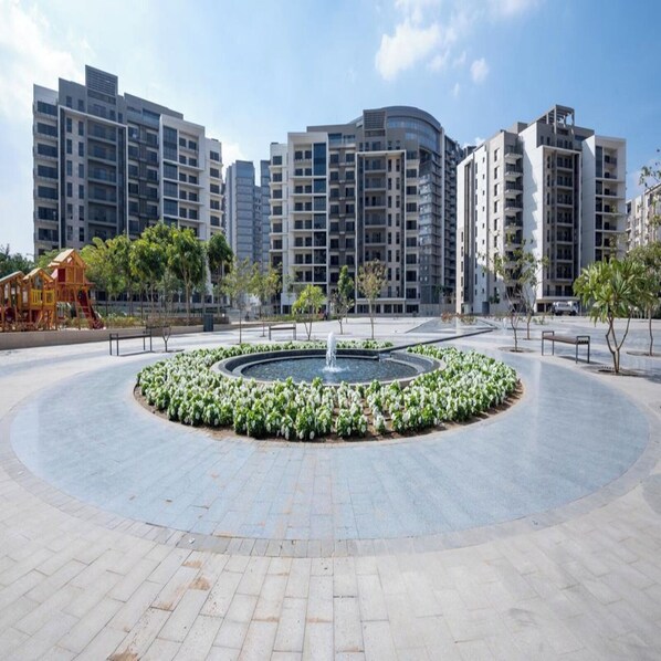A modern residential complex with high-rise buildings, a central circular plaza with a fountain, and a playground. - Easy Rental (Sheikh Zayed City)