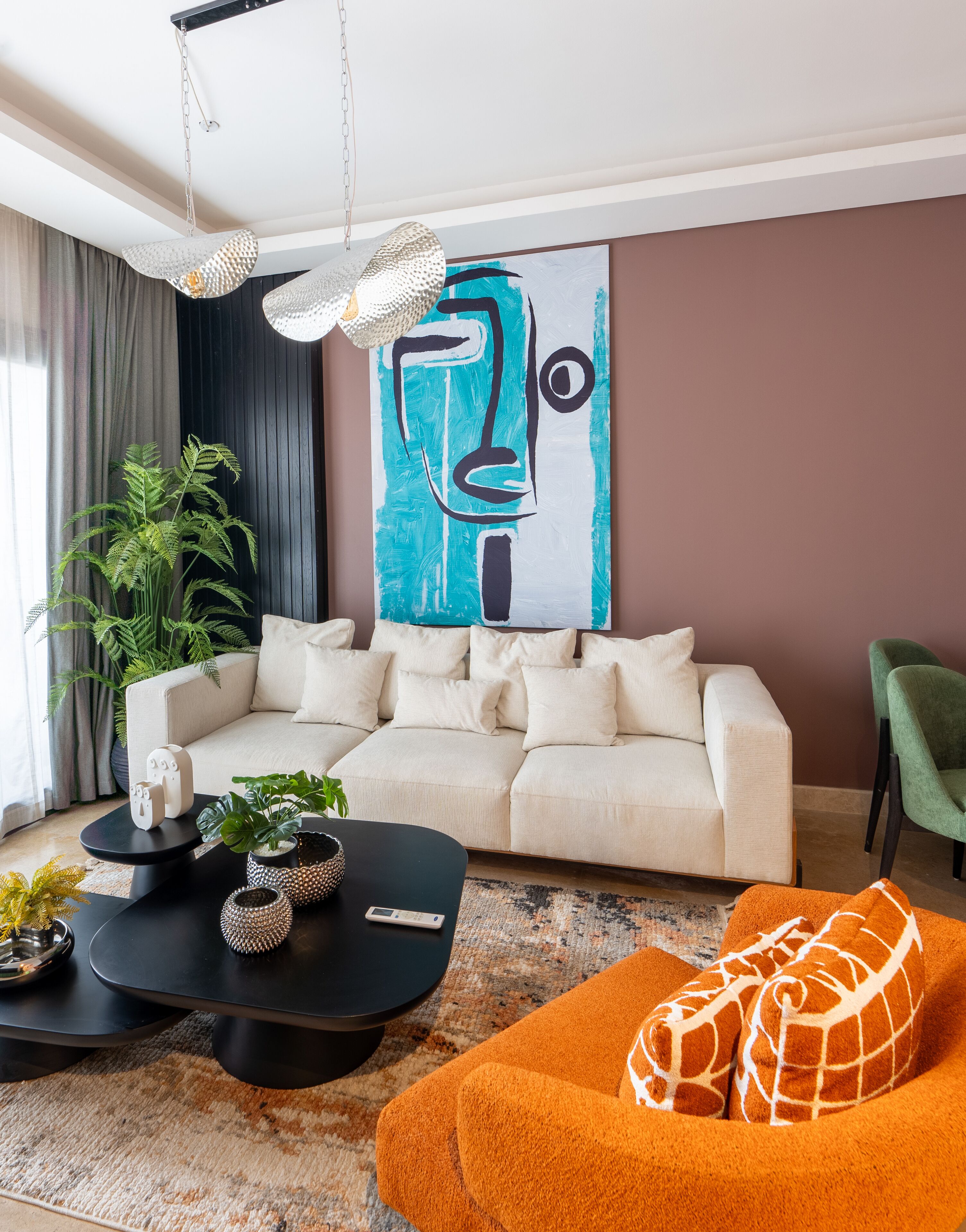 A modern living room with a beige sofa, a black coffee table, and an orange pouf. There's a large abstract painting on the wall and a potted plant on the left.