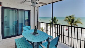 A balcony with a table and chairs, a statue, and a view of the beach. - Seaside 406 | Renovated Beachfront, Pool, Beach Access + Views! (Fort Myers Beach)