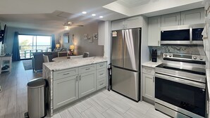 A modern kitchen with stainless steel appliances, a marble countertop, and a view to the outside. - Seaside 406 | Renovated Beachfront, Pool, Beach Access + Views! (Fort Myers Beach)