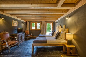 A cozy room with a bed, a chair, a small table, and a cabinet. There are windows with curtains and a view of greenery outside. - Les Rives d'Argentière (Chamonix-Mont-Blanc)