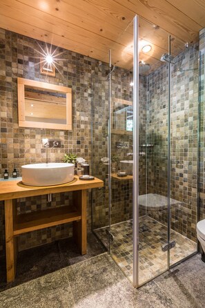 A modern bathroom with a stone mosaic backsplash, a wooden vanity, a glass-enclosed shower, and a round sink. - Les Rives d'Argentière (Chamonix-Mont-Blanc)
