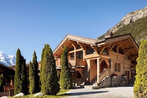 A wooden chalet with a balcony, surrounded by tall trees and a mountain backdrop. - Les Rives d'Argentière (Chamonix-Mont-Blanc)