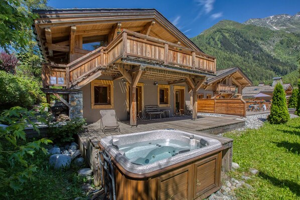 A wooden chalet with a hot tub, stone walls, and a balcony overlooking a mountainous landscape. - Les Rives d'Argentière (Chamonix-Mont-Blanc)