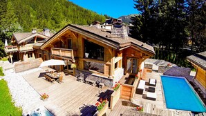 A wooden cabin with a deck, outdoor seating, and a swimming pool. - Les Rives d'Argentière (Chamonix-Mont-Blanc)