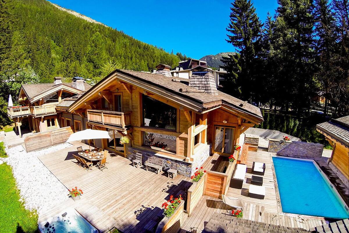 A wooden cabin with a deck, outdoor seating, and a swimming pool.