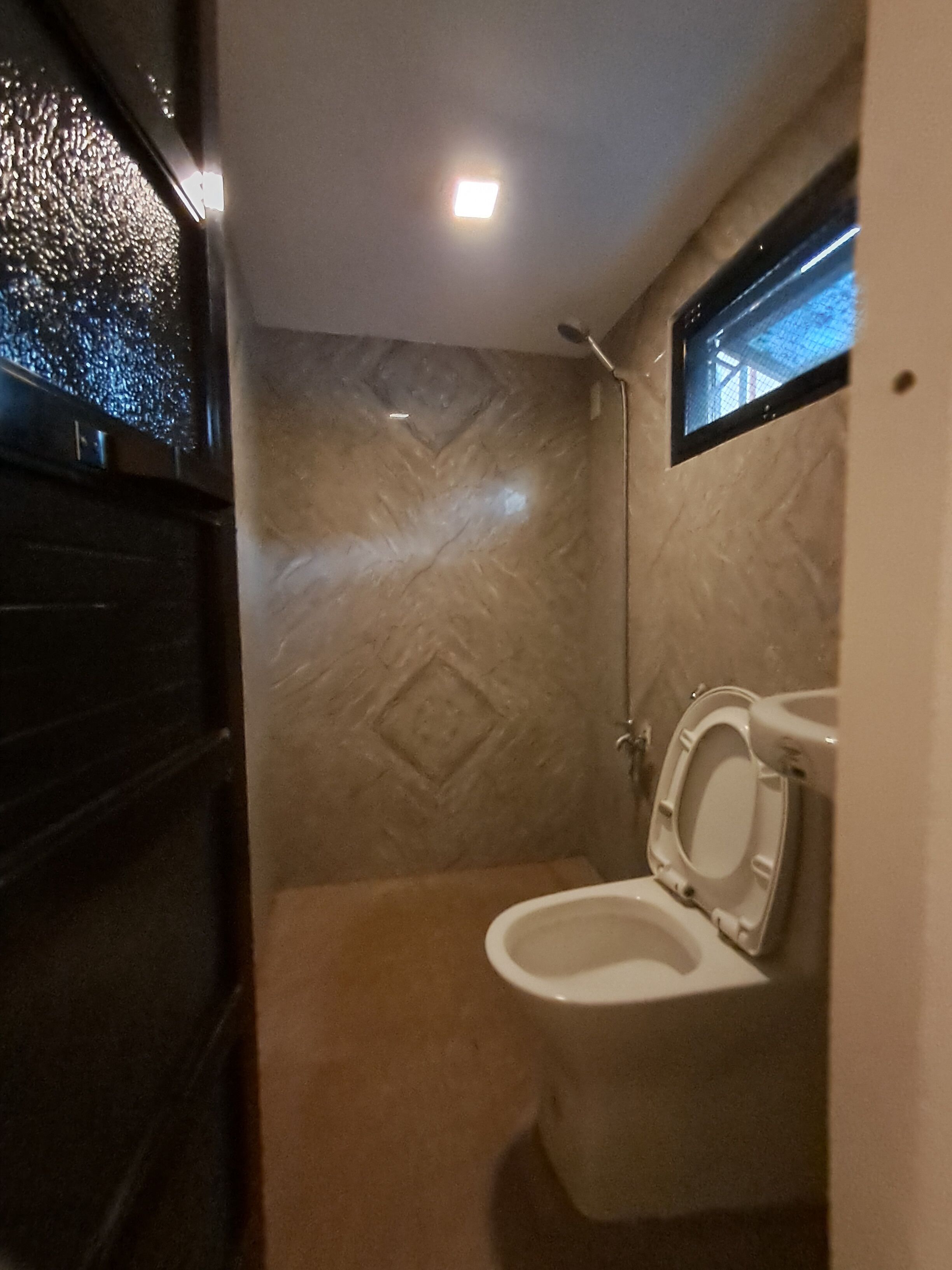 A small bathroom with a toilet, a shower, and a window.