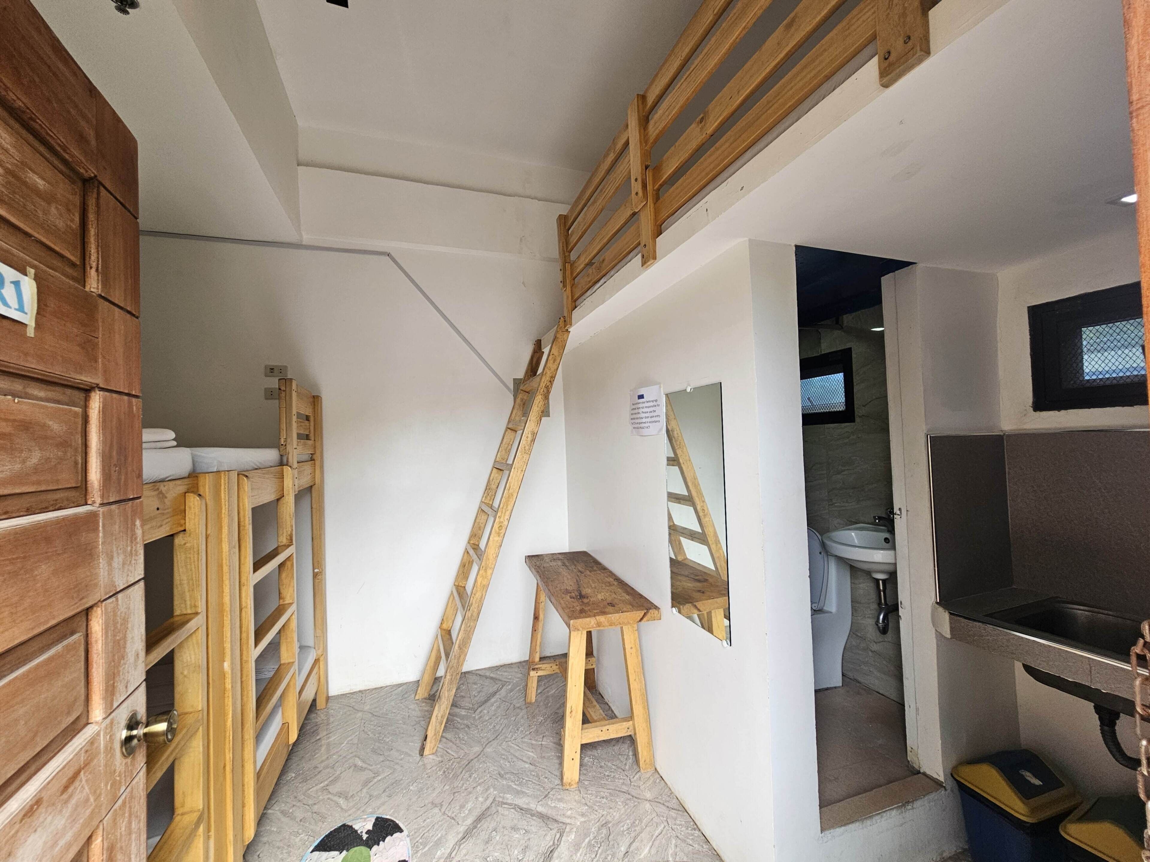 Ein kleiner Raum mit einer Holzbank, einer Klapptreppe, einem Waschbecken und einem kleinen Tisch.