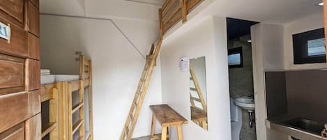 Ein kleiner Raum mit einer Holzbank, einer Klapptreppe, einem Waschbecken und einem kleinen Tisch.
