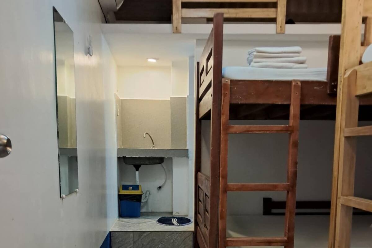 A bunk bed room with a wooden ladder, a small sink, and a mirror on the wall.