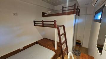 A bunk bed with a wooden frame, a ladder, and a white mattress. There is a small white chair and a pet bed in the corner.