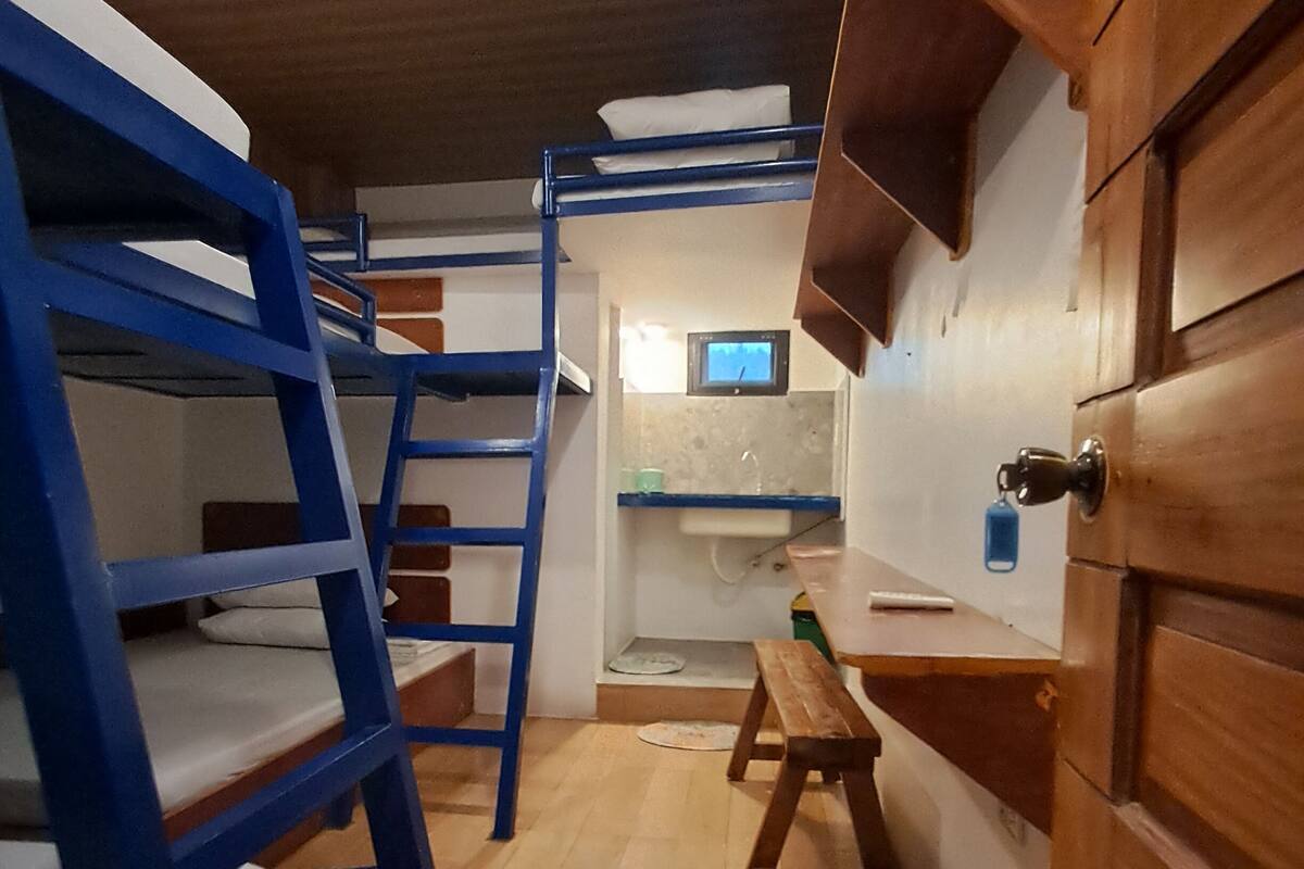 A bunk bed room with a wooden desk and a small bathroom.