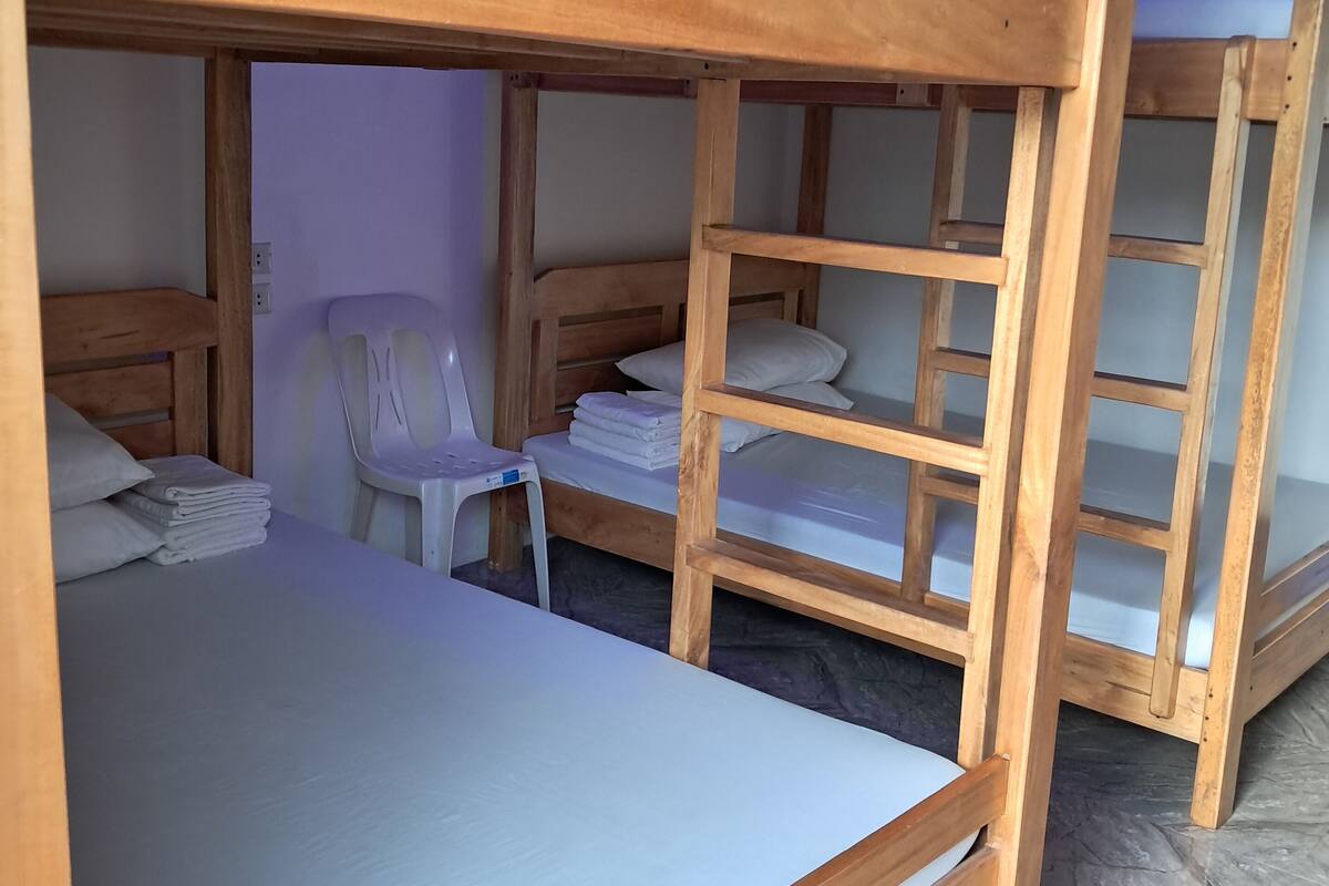 A bunk bed room with a wooden frame, a white chair, and neatly folded towels.