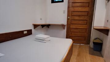 A small, clean room with a bed, a wooden door, a small window, and a wall-mounted air conditioner.