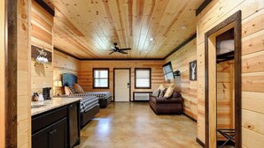 A log cabin interior with a kitchen, two beds, a brown leather sofa, and a ceiling fan. - Big Timber Lodge (Broken Bow)