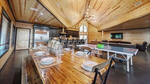 A spacious dining area with a long wooden table set for a meal, a ping pong table, and a television in the background. - Big Timber Lodge (Broken Bow)