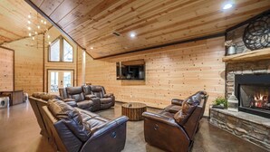 A cozy log cabin interior with a fireplace, leather sofas, and a stone fireplace surround. - Big Timber Lodge (Broken Bow)
