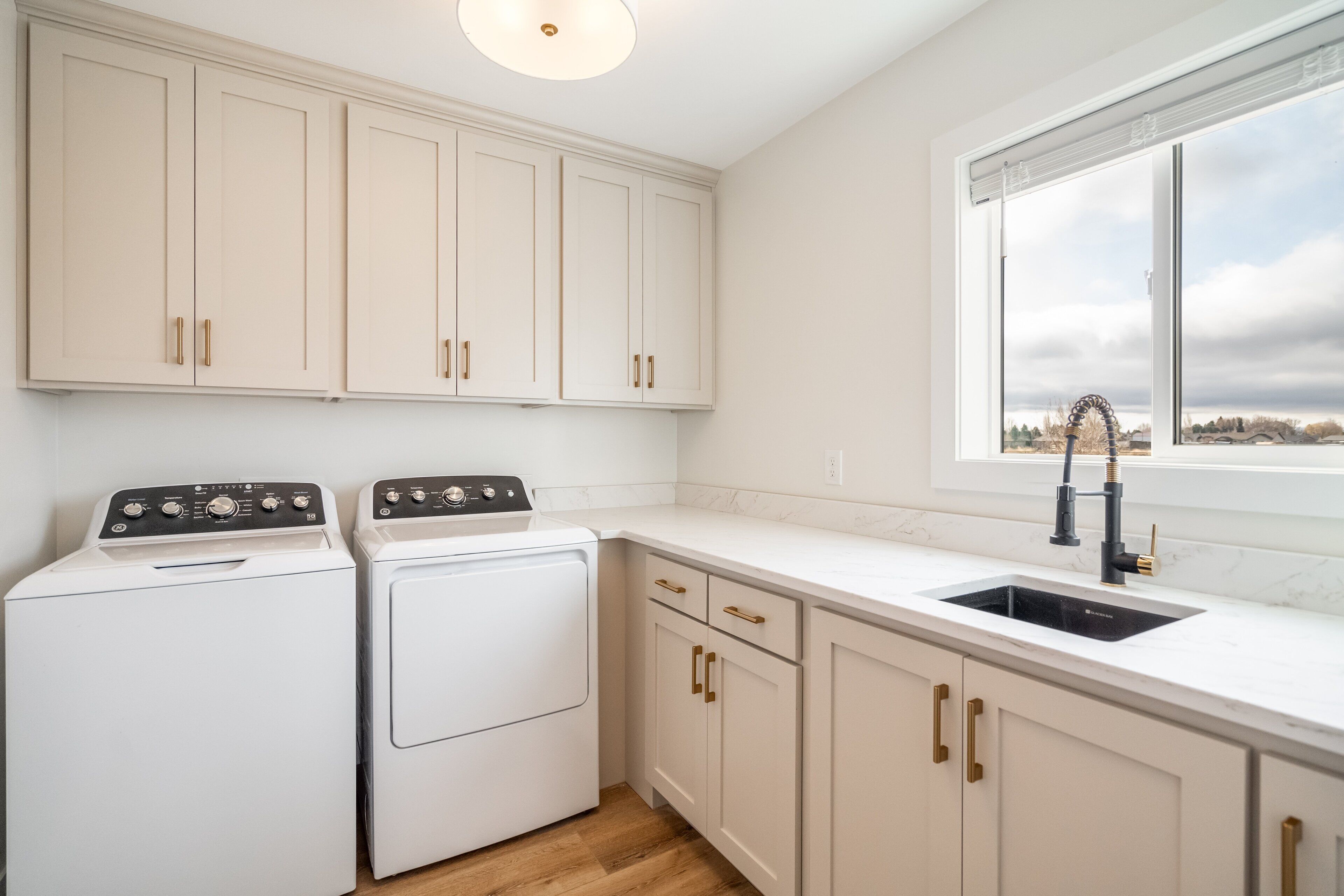Una cocina con armarios blancos, horno doble, pileta y ventana con vista al exterior.