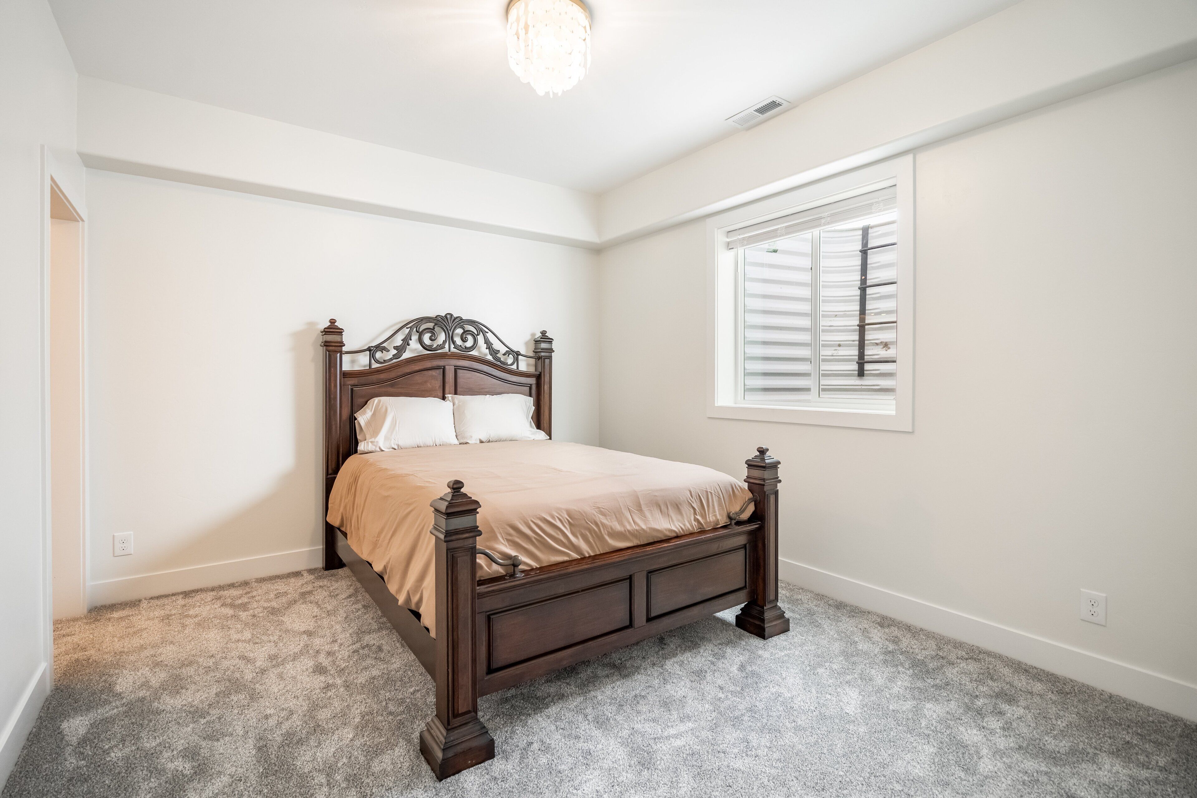 A bedroom with a wooden bed, a window with blinds, and a carpeted floor.
