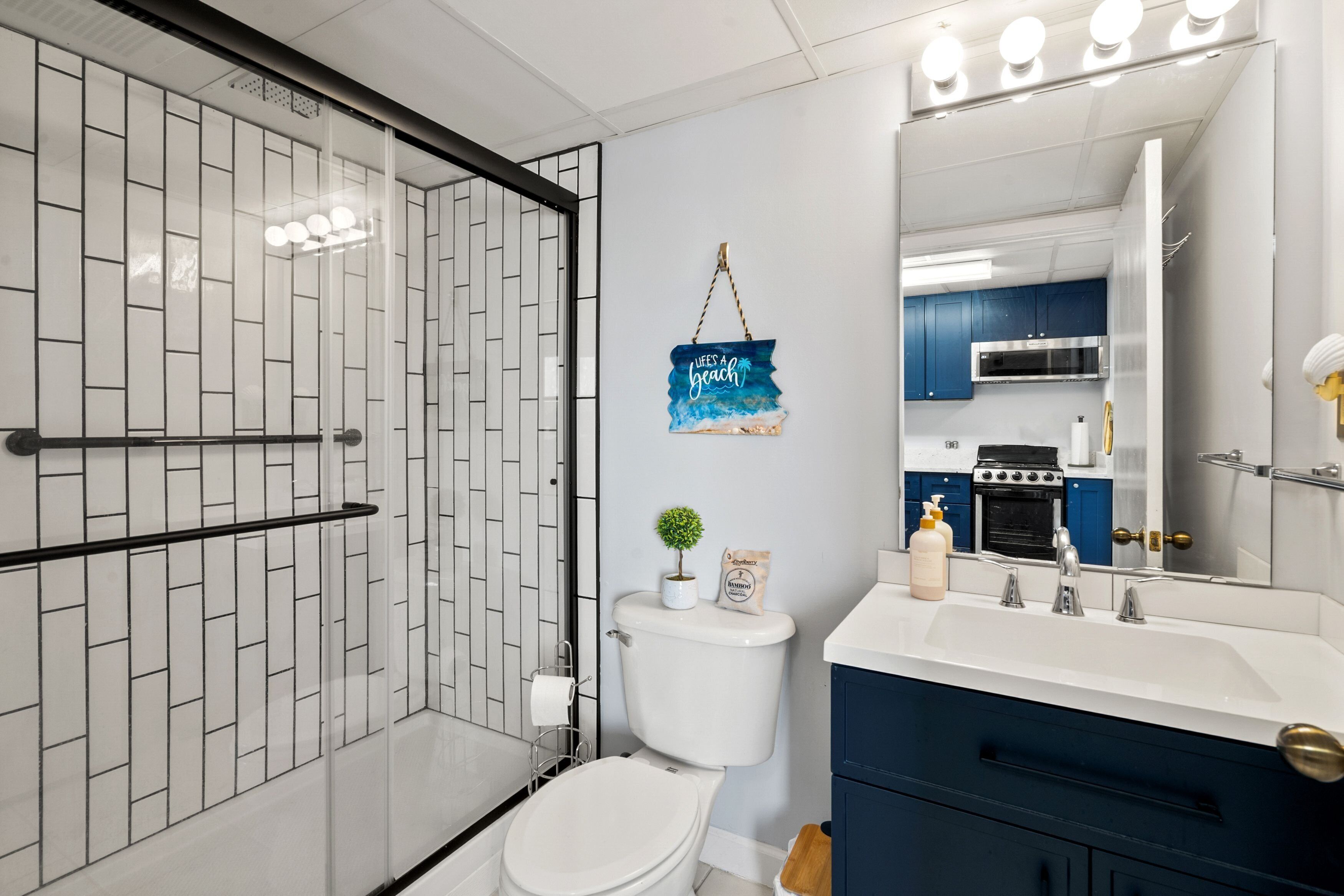 Un baño moderno con cabina de ducha de vidrio, inodoro, lavabo con espejo y un cartel decorativo.