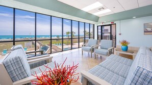 Un vestíbulo de hotel con grandes ventanales, vista a la piscina y zonas de estar.