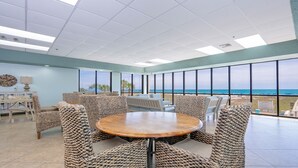 Una habitación amplia con una mesa redonda y sillas de mimbre, ventanas grandes con vista al océano e iluminación empotrada en el techo.