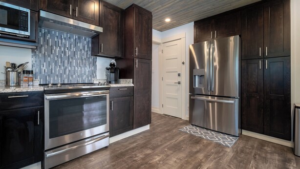 A modern kitchen with dark wood cabinets, stainless steel appliances, and a tiled backsplash. - Multi-level home, large wrap around deck, stunning views of the Necanicum River. (Seaside)
