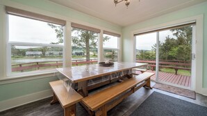 A spacious room with a large wooden table and benches, large windows with a view of a park and buildings, and a chandelier. - Multi-level home, large wrap around deck, stunning views of the Necanicum River. (Seaside)