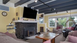 A living room with a stone fireplace, a flat-screen TV, and a large window offering a view of the outdoors. - Multi-level home, large wrap around deck, stunning views of the Necanicum River. (Seaside)