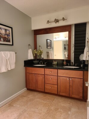 Une salle de bain avec un double lavabo, des meubles en bois, un grand miroir et un tableau encadré au mur.