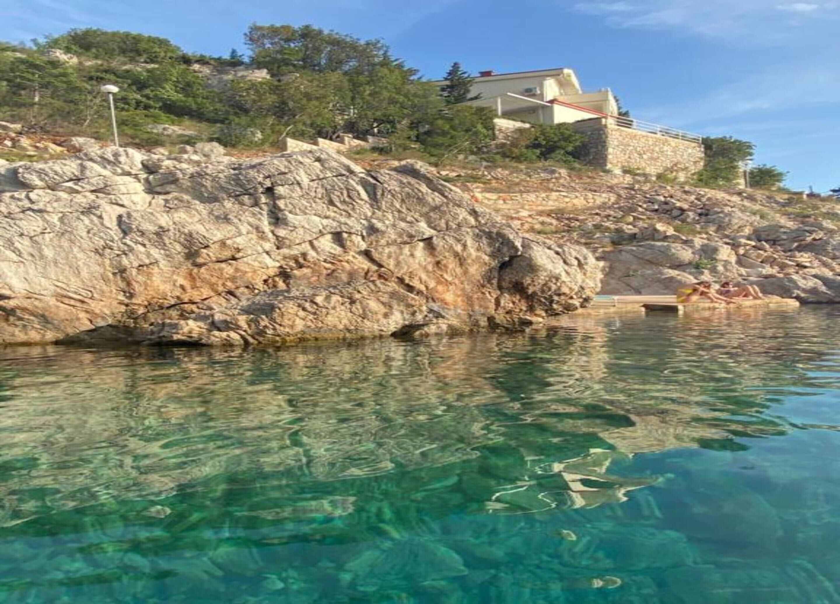 A coastal scene with clear water, rocky terrain, and a building on a hill.
