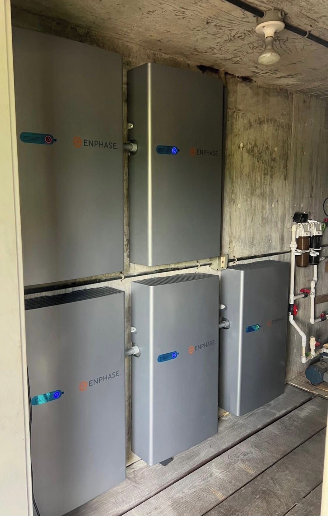 Four ENPHASE refrigerators stacked in a corner with visible pipes and a ceiling fan.