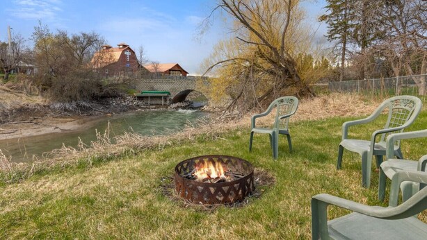 A riverside setting with a fire pit, chairs, and a rustic building in the background. - Pet Friendly Home with Fishing Access and Fire Pit (Kalispell)