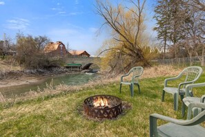 A riverside setting with a fire pit, chairs, and a rustic building in the background. - Pet Friendly Home with Fishing Access and Fire Pit (Kalispell)