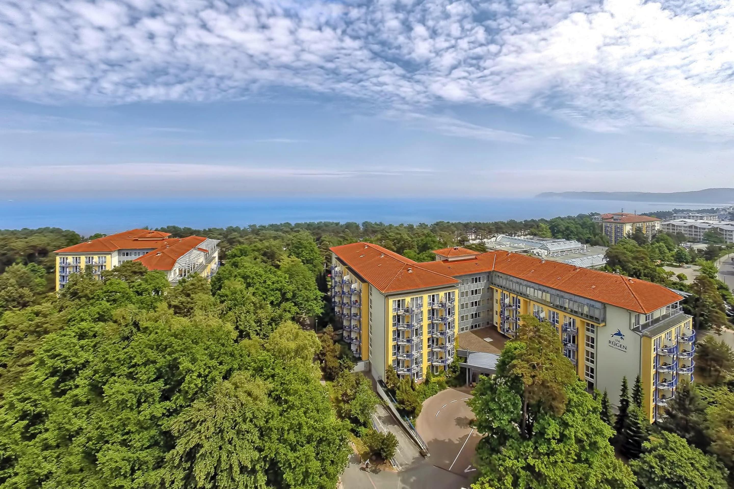 A multi-story hotel with balconies, surrounded by greenery and a view of the sea.