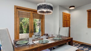 Un comedor con una mesa de madera dispuesta para cuatro personas, un banco y vista al jardín a través del ventanal.